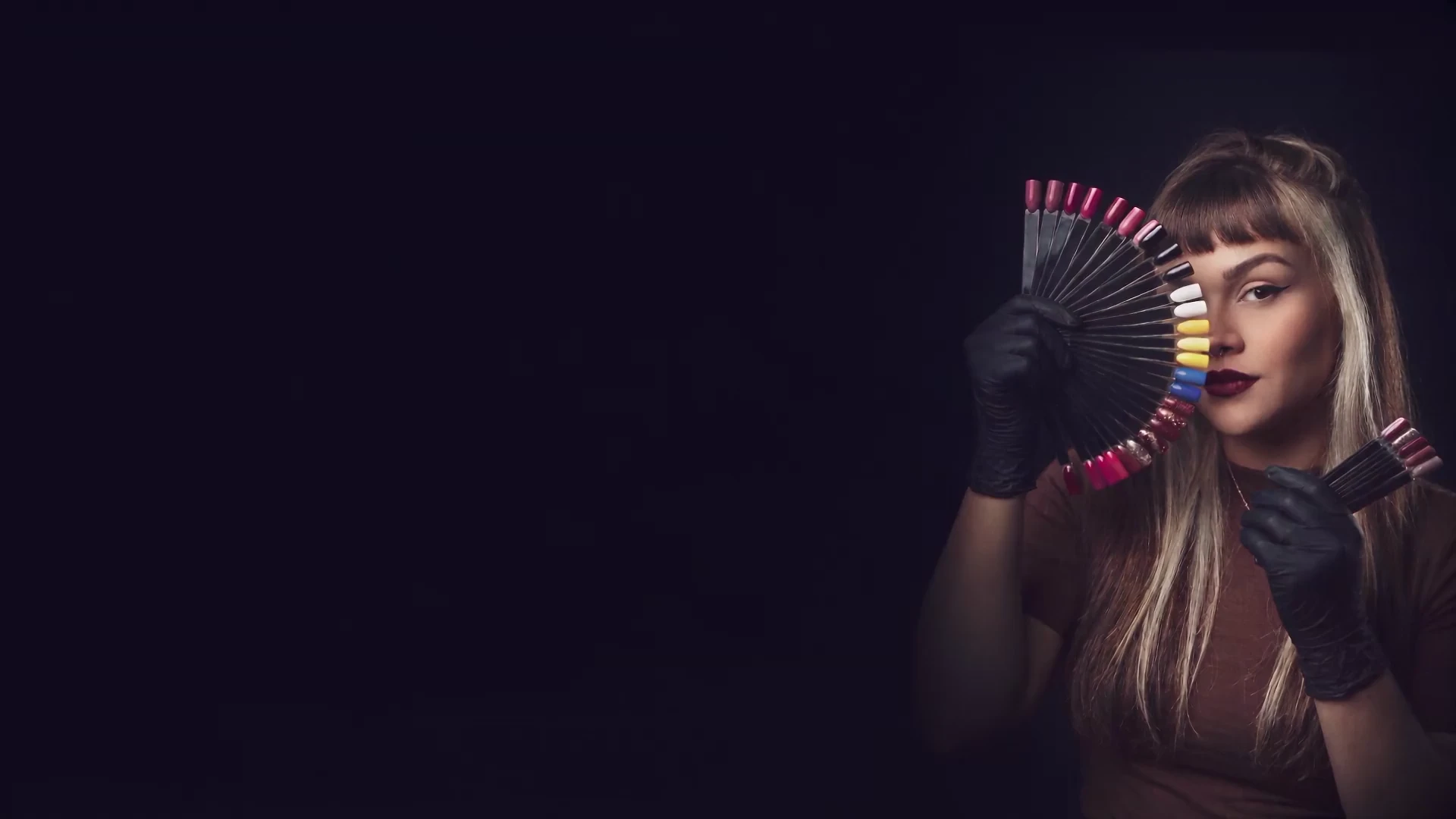 Carolina Schiminski com leques de cores de unhas, luvas pretas e maquiagem em tons de vinho